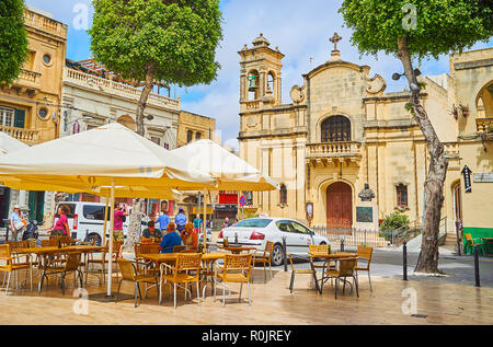 VICTORIA, Malta - 15 giugno 2018: la facciata di San Jacob Chiesa dietro gli ombrelli di ristorante all'aperto in Piazza Indipendenza, il 15 giugno a Victoria. Foto Stock