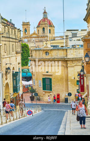 VICTORIA, Malta - 15 giugno 2018: la strada collinare si apre la vista sulla cupola rossa e i campanili di St George Basilica sorge dietro il consiglio locale b Foto Stock