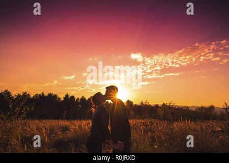 Giovane baciare e tenendo le mani in natura tramonto Foto Stock