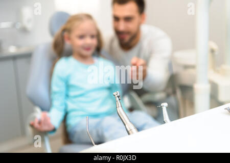 Close-up shot di dentista strumenti sul piedistallo con sfocato padre e figlia sullo sfondo Foto Stock