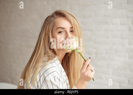 Close-up giovane donna caucasica holding bouquet di fiori, guarda attraverso la finestra con il sorriso sulla faccia in piedi nella stanza di luce in ambienti interni Foto Stock