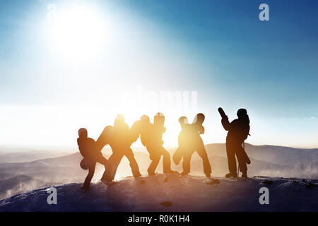 Gruppo di amici felici gli sciatori e gli snowboarder si divertono. Cinque sagome con sci e snowboard sulla cima della montagna a stazione sciistica Foto Stock