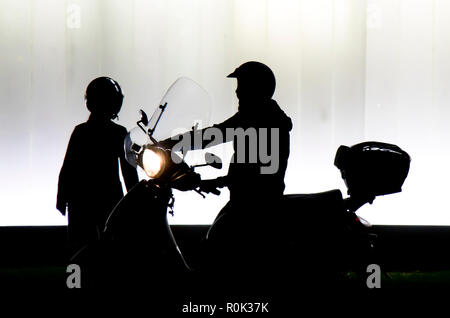 Sfocata silhouette di due persone in partenza su una moto di fronte all edificio moderno in sella a una motocicletta con faro su nella notte in bianco e nero e w Foto Stock