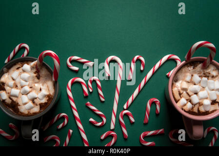 Due tazze di cioccolata calda con mini marshmallows e candy canne di diverse dimensioni su un tavolo verde, direttamente sopra visualizza Foto Stock