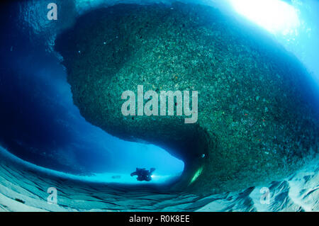 Nuoto subacqueo intorno ad una grande formazione di roccia in una grotta aperta sul costo della Sardegna. Foto Stock