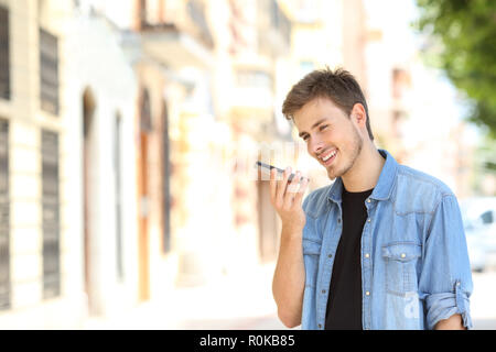 Happy boy utilizzando il riconoscimento vocale su uno smartphone in strada Foto Stock