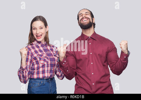 Ritratto di felice stupito uomo barbuto con nero capelli raccolti e la donna in uno stile informale in piedi con pugno e celebrare la loro vittoria. prigioniero al coperto Foto Stock