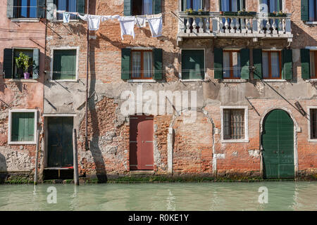 Vecchi edifici in mattoni e dipinto di persiane verdi con il bianco biancheria stesa ad asciugare su un canal Venezia Italia Foto Stock