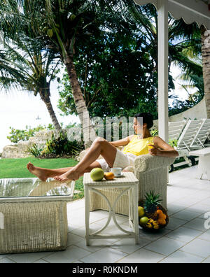 Giovane donna rilassante in bianco poltrona in vimini, terrazza, giardino tropicale, palme, Guadalupa, French West Indies, Foto Stock