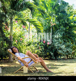 Giovane donna napping in sedia a sdraio, giardino tropicale, Guadalupa, French West Indies, Foto Stock