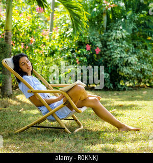 Giovane donna napping in sedia a sdraio, giardino tropicale, Guadalupa, French West Indies, Foto Stock