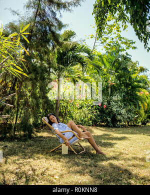 Giovane donna napping in sedia a sdraio, giardino tropicale, Guadalupa, French West Indies, Foto Stock