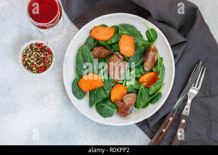 Warm insalata di spinaci con fegato di pollo e zucca cotta al forno. Una deliziosa cena con vino rosso per i buongustai. Messa a fuoco selettiva, vista dall'alto Foto Stock