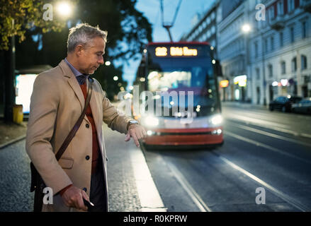 Imprenditore maturo con la valigia in attesa di un tram in serata. Foto Stock