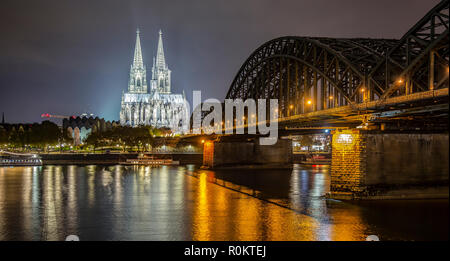 La cattedrale di Colonia illuminata di notte con il fiume Reno e il ponte di Hohenzollern visibile Foto Stock