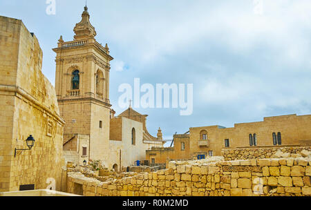 La vista sul campanile della cattedrale dell Assunzione della vecchia strada stretta di Rabat cittadella con un rovine del muro di pietra sul primo piano, Victoria, Goz Foto Stock