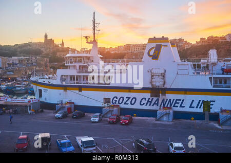 GHAJNSIELEM, Malta - 15 giugno 2018: gli ultimi raggi del tramonto oltre il Mgarr harbour con una vista sul traghetto ro-ro in primo piano, il 15 giugno a G Foto Stock