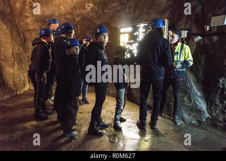 Un gruppo di visitatori che indossa caschi di sicurezza, raccogliere attorno alla loro guida in un alta vis jacket, mostrando un illuminato di mappa della metropolitana di caverna nel sistema Foto Stock