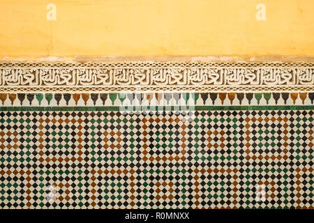 La colorata Vecchia giallo marocchino parete dipinta con una banda di calligrafia islamica al di sopra di zellige tilework. Foto Stock