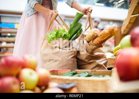 Close-up di un irriconoscibile donna in gonna in piedi in cibo negozio organico e la raccolta della spesa pesanti sacchi pieni di prodotti Foto Stock