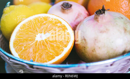 Melograni, di arance e di limoni in un empio cesto su un tavolo in legno di una cucina rustica. Autunno sfondo con la copia in bianco lo spazio per l'editor di testo. Foto Stock