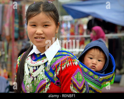 Giovane vietnamita Flower H'mongs hill-tribe donna con lentiggini porta un simpatico baby boy in un tradizionale ricamato fionda bambino sulla schiena. Foto Stock