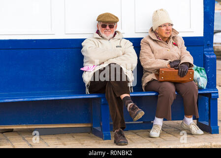 Coppia senior seduta sul banco vicino al molo a Swanage, Dorset Regno Unito nel mese di novembre Foto Stock