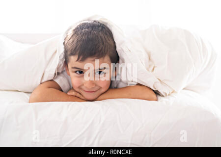 Un simpatico quattro anni ragazzo in biancheria da letto bianca Foto Stock