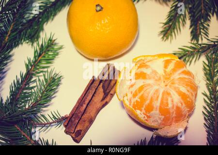 Due i mandarini, uno dei quali è sbucciata, giacciono su uno sfondo bianco. Intorno i mandarini sono rami di abete e un paio di bastoncini di cannella fragrante. Foto Stock