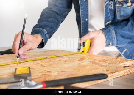 Carpenter operando con cautela guardando i piani di lavoro in falegnameria. Egli è imprenditore di successo al suo posto di lavoro. martellare un chiodo supporta sulla build Foto Stock