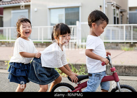 Ritratto di due ragazze giapponesi e ragazzo giocando sulla strada con una bicicletta, sorridente alla fotocamera. Foto Stock