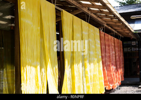 Tinti di fresco di colore giallo brillante e di colore arancione in tessuto da appendere al di fuori di un impianto tessile officina di colorante. Foto Stock