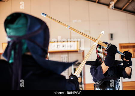 Due giapponesi combattenti di Kendo di indossare le maschere di Kendo di praticare il legno con la spada in palestra. Foto Stock