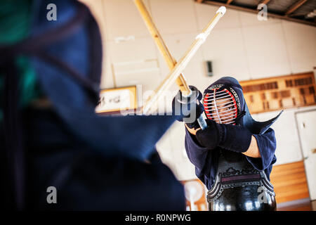 Due giapponesi combattenti di Kendo di indossare le maschere di Kendo di praticare il legno con la spada in palestra. Foto Stock