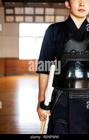 Maschio di Kendo giapponese fighter in piedi in una palestra, tenendo la spada di legno. Foto Stock