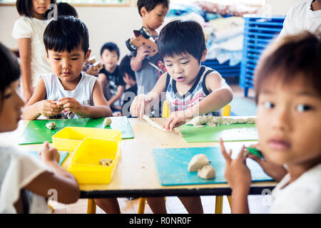 Un gruppo di bambini seduti a tavola in un giapponese di età prescolare, fare artigianato.. Foto Stock