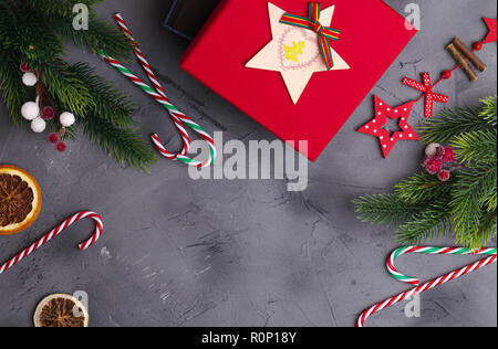 Rami di abete su calcestruzzo sfondo grigio con confezione regalo rossa e decorazioni. Natale e Anno Nuovo. Lay piatto. Foto Stock