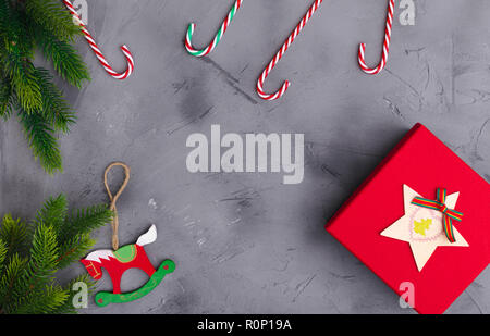 Rami di abete su calcestruzzo sfondo grigio con confezione regalo rossa e decorazioni. Natale e Anno Nuovo. Lay piatto. Foto Stock