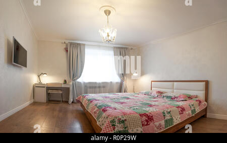 Moderno appartamento in tenui colori caldi, interno, camera da letto. Letto, tavolo, TV Foto Stock