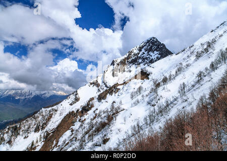 Bella coperta di neve Aibga picco di montagna sul cielo blu con nuvole di sfondo. Drammatico paesaggio panoramico delle montagne del Caucaso, Sochi, Russia Foto Stock