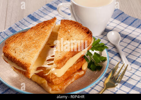 Fette biscottate di pane con il formaggio e il prezzemolo verde sulla piastra bianca, forcella, una tazza di caffè e cucchiaio con cucina blu igienico. La buona cucina per la prima colazione Foto Stock