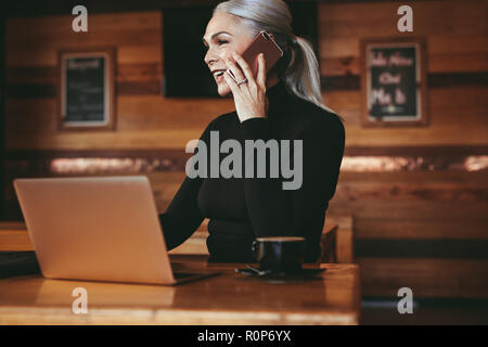 Bella senior imprenditrice seduta presso il cafe avente conversazione telefonica con il cliente. Femmina matura professionista business parlando al telefono cellulare Foto Stock