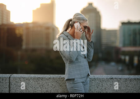 Ritratto di senior imprenditrice in piedi sul ponte aperto e parlando al telefono cellulare. Coppia professionista business parlando al cellulare outdoo Foto Stock