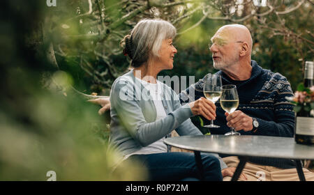 Il vecchio uomo e donna di trascorrere del tempo insieme a bere vino. Vecchia coppia seduti insieme in un giardino azienda bicchieri da vino guardando ogni altro. Foto Stock