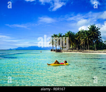 Giovane donna in costume da bagno rosso a prendere il sole su giallo aria materasso, galleggiante sul Mare dei Caraibi, spiaggia tropicale, palme, Guadalupa, French West Indies, Foto Stock