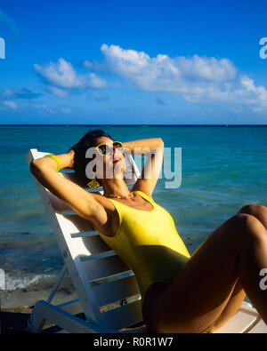 Giovane donna con il costume da bagno giallo sole e rilassarsi in prendisole, spiaggia tropicale, il mare dei Caraibi, Guadalupa, French West Indies, Foto Stock