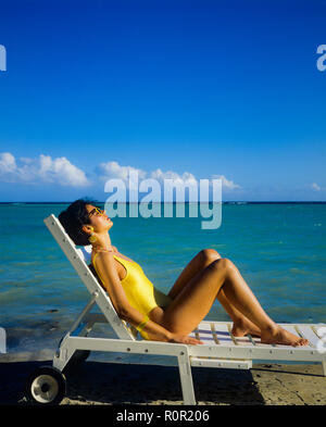 Giovane donna con il costume da bagno giallo sole e rilassarsi in prendisole, spiaggia tropicale, il mare dei Caraibi, Guadalupa, French West Indies, Foto Stock