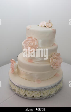 Tre livelli di bianco ghiacciato torta nuziale con crema e nastro rosa pallido fiori ghiacciata decorare la torta Foto Stock