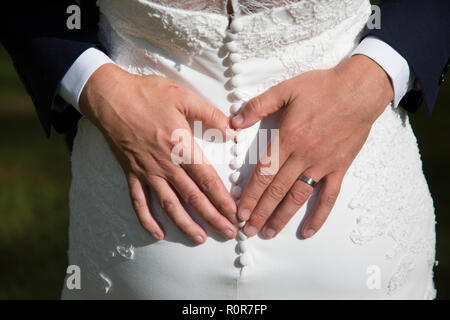 Lo sposo facendo una forma di cuore dietro le spose indietro con le sue mani su di loro giorno delle nozze, mostrando anche fuori dal suo nuovo wedding band Foto Stock