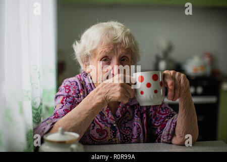 Ritratto di una donna anziana seduta al tavolo e le bevande il tè. Foto Stock